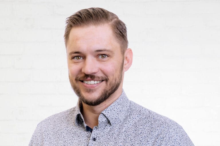Porträt des IT-Consultants und Key Account Managers Stefan Milde vor einer neutralen Wand aus weißen Backsteinen.