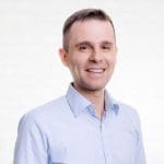 Portrait of the managing director Thomas Kutzschbach in front of a neutral wall made of white bricks.