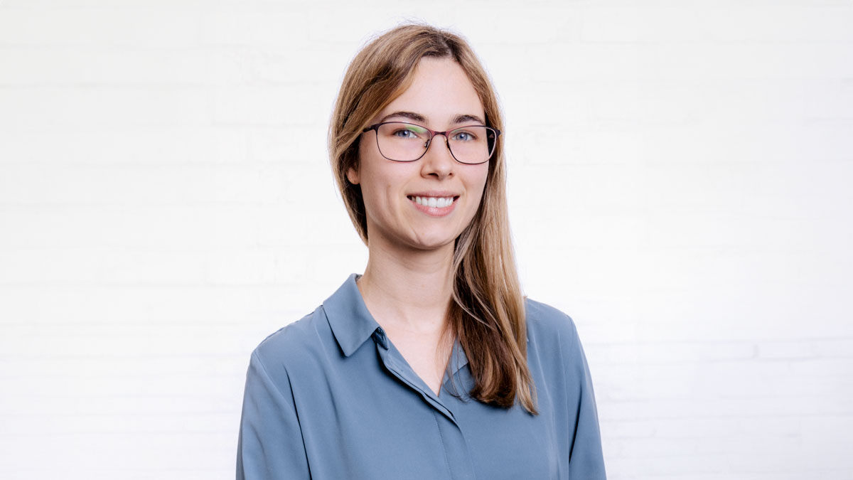 Porträt von Lara Wiedemann aus dem Onlinemarketing vor einer neutralen Wand aus weißen Backsteinen.
