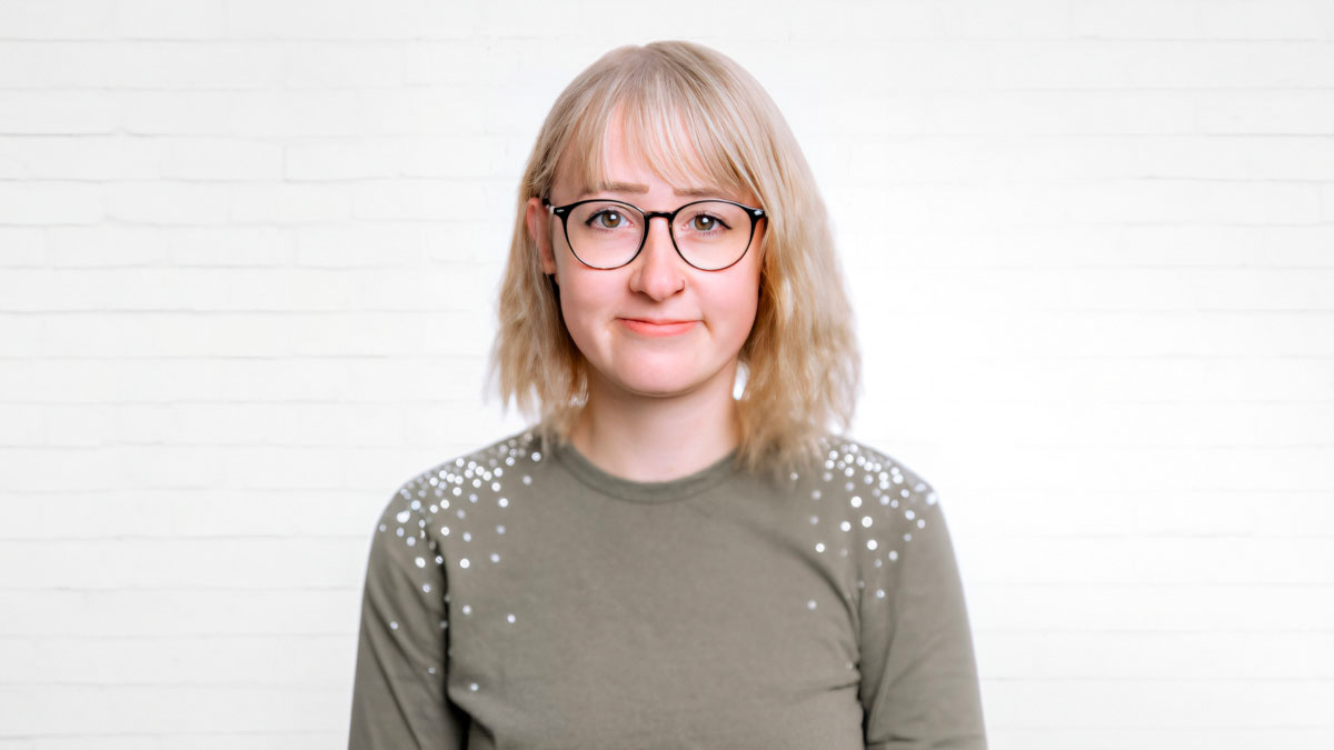 Porträt der Projektmanagerin Lisa Marie Schuster vor einer neutralen Wand aus weißen Backsteinen.