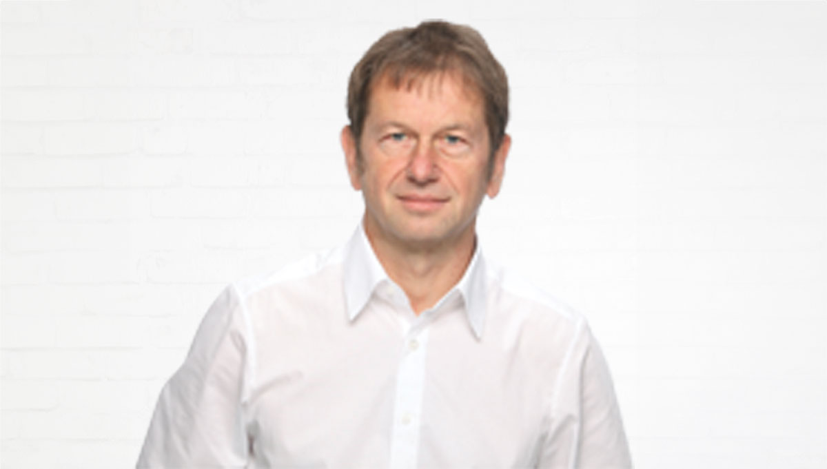 Porträt des Systemtechnikers Peter Gruschka vor einer neutralen Wand aus weißen Backsteinen.