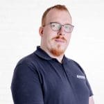Porträt des Systems Engineers Steve Lang vor einer neutralen Wand aus weißen Backsteinen.