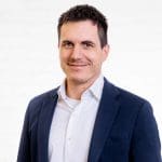 Porträt des Senior Systems Engineers Thomas Stach vor einer neutralen Wand aus weißen Backsteinen.