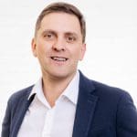 Porträt des Prokuristen und Leiter Technik Tobias Schiffelholz vor einer neutralen Wand aus weißen Backsteinen.