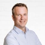Porträt des Geschäftsleiters und Prokuristen Christian Fischer vor einer neutralen Wand aus weißen Backsteinen.