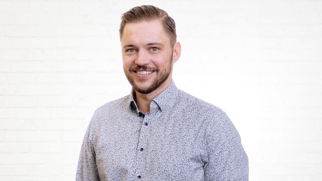 Porträt des IT-Consultants und Key Account Managers Stefan Milde vor einer neutralen Wand aus weißen Backsteinen.