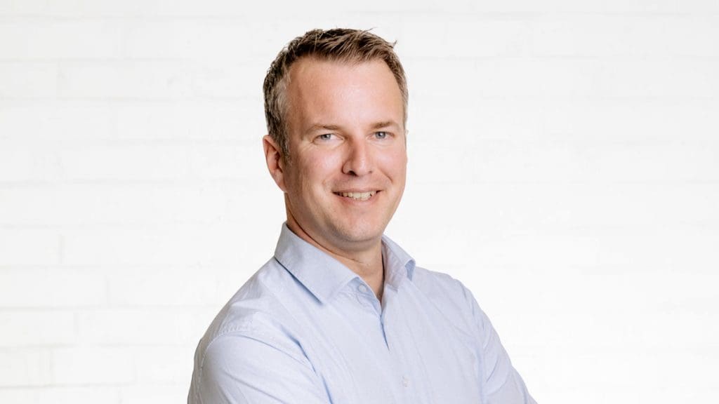 Porträt des Geschäftsleiters und Prokuristen Christian Fischer vor einer neutralen Wand aus weißen Backsteinen.