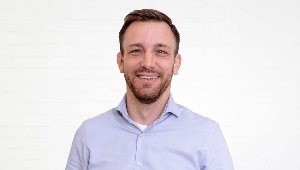 Porträt des IT-Consultants Johannes Dorn vor einer neutralen Wand aus weißen Backsteinen.