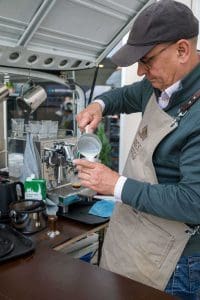 Barista mit Schürze gießt Milch in einen Kaffeebecher an der Kaffee Ape beim Kutzschbach Partnertag 2025