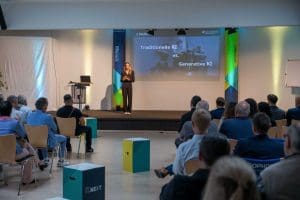 Frau hält Vortrag zum Thema 'Traditionelle KI vs. Generative KI' beim Kutzschbach Partnertag 2025 vor sitzendem Publikum in modernem Veranstaltungsraum